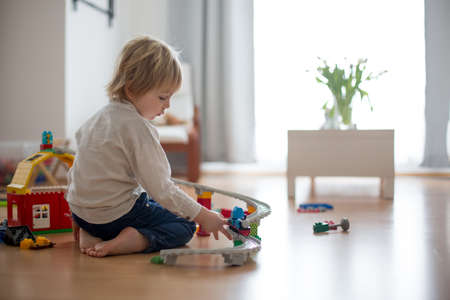 Cute child, playing with colorful toy blocks. Little boy building house of block toys sitting on the floor in sunny spacious bedroom. Educational game for toddlersの写真素材