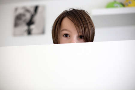 Cute child, hiding in bed, only eyes peeping out above the wooden board in the morningの写真素材