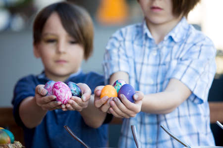 Sweet children, brothers, coloring and paiting eggs for Easter in garden, outdoors at home in backyardの写真素材