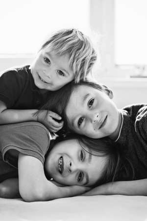 Three beautiful children, boy brothers, having family portrait, hugging, lying in bedの写真素材