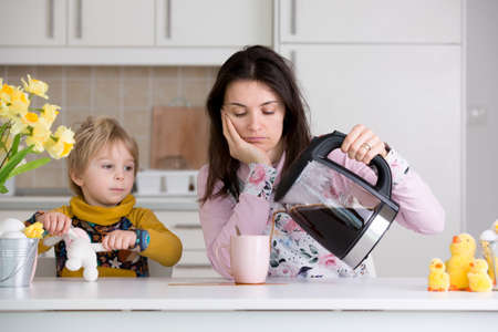 Tired mother, trying to pour coffee in the morning. Woman lying on kitchen table after sleepless night, trying to drink coffeeの写真素材