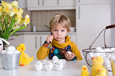 Toddler child, boy, drawing funny emoticons on easter eggs with black pen
