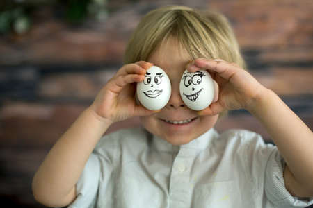 Cute child, holding white eggs with emotions drawn on them for Easter, funny faces