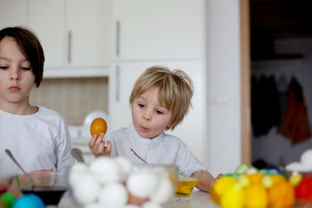 Children, boy siblings, coloring eggs for Easter at home
