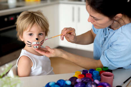 Mother painting on little blond toddler boys' face easter bunny at home