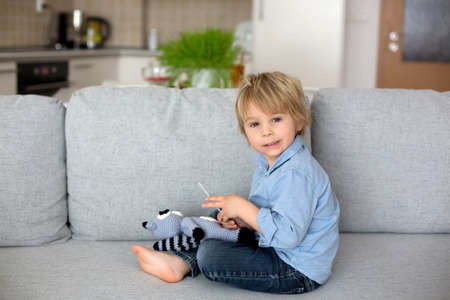 Little todller child, boy, playing with knitted toy, pretending to making swab antigen covid test to...