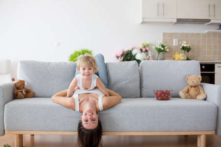 Mother and toddler child, hanging upside down from a couch at home, smiling happilyの写真素材