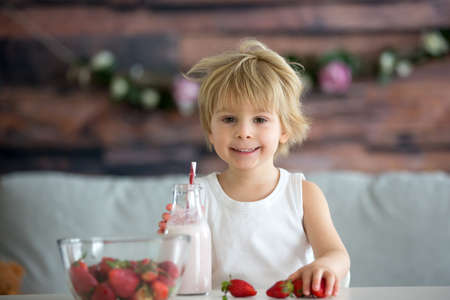 Cute toddler child, blond boy, drinking smoothie and easting strawberries at homeの写真素材