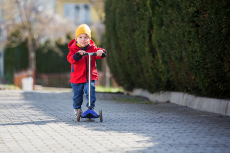 Child, toddler boy, riding scooter in the park, springtime