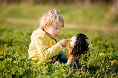 Little toddler blond child, boy, playing with handknitted doll in the parkの写真素材