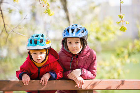 Children, brothers, riding scooters in the park together, spring sunny dayの写真素材
