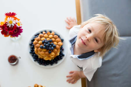 Sweet toddler child, boy, eating bubble waffles with fruits at home for breakfast, flowers on the...