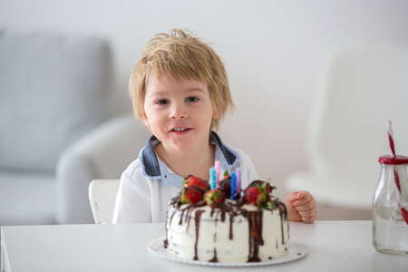 Four years old blond child, preschool boy, celebrating birthday at home with homemade cake with...