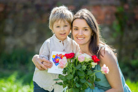 Beautiful kid and mom in spring park, flower and present. Mother getting gift from toddler boy for Mothers day in beautiful gardenの写真素材