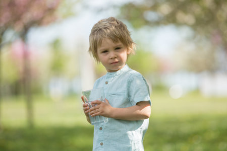 Beautiful blond child, boy, drinking water in the park on a hot summer day