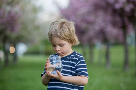 Beautiful blond child, boy, drinking water in the park on a hot summer day