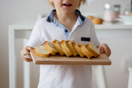Child, blond toddler boy, holding wooden cutting board with homemade ciabatta bread, serving at homefreshlz baked breadの写真素材