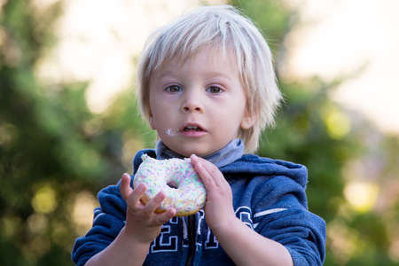 Cute child, eating donnuts in garden, smilingの写真素材