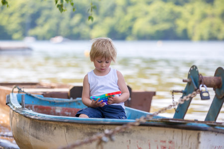Little toddler child, blond boy, playing with pop it antistress toy in the park in a boat in lakeの写真素材