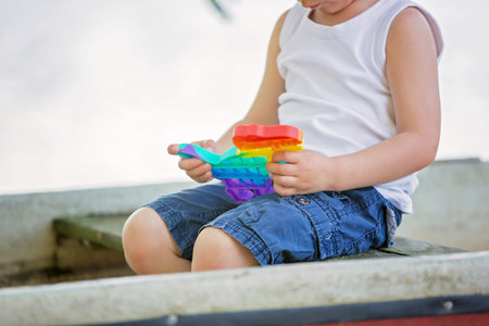 Little toddler child, blond boy, playing with pop it antistress toy in the park in a boat in lakeの写真素材