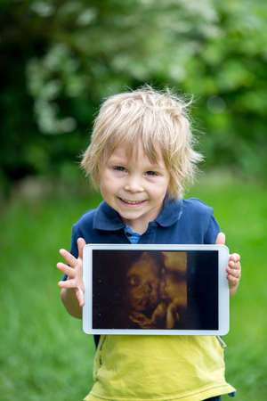 Cute toddler child, holding a picture of his little unborn baby sister from the ultrasoundの写真素材