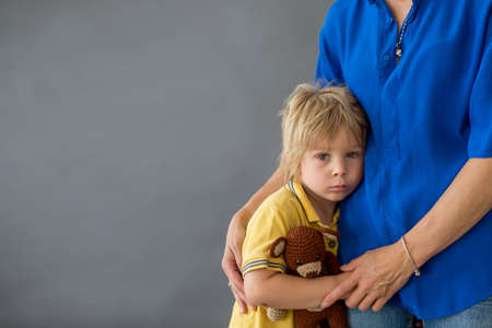 Sad little child, blond boy, hugging his mother at homeの写真素材