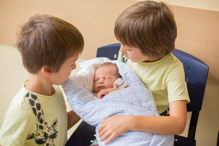 Two boys, brothers, meeting for the first time their new baby brother at hospital. Family happiness conceptの写真素材