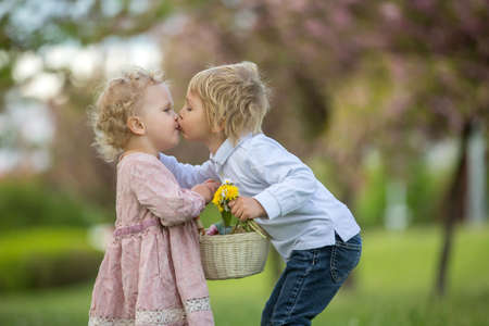 Beautiful children, toddler boy and girl, playing together in cherry blossom garden, boy giving a little bouquet of wild flowers to the girl. Kids friendship, happy childhoodの写真素材