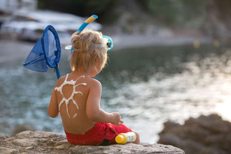 Little toddler child, holding sun cream, applying it on his body, sun protection during summer vacationの写真素材