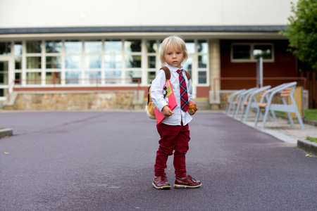 Preschool blond child, cute boy in uniform, hodling apple and book, going in preschool for the first time after summer vacationの写真素材