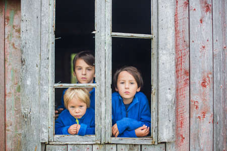 Sad children, looking out of the window of old ruined building in Norway