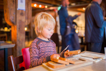 Preschool child, cute boy, eating bread in a restaurant, cozy atmosphere, local small restaurant in Tromso, Northern Norwayの写真素材
