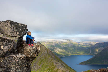 Cute child, standing on a rock and looking over Segla mountain on Senja island, North Norway. Amazing beautiful landscape and splendid nature in scandinavian country Norwayの写真素材