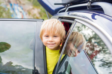 Cute blond child, looking out of the window of a car, reflection on the windowの写真素材