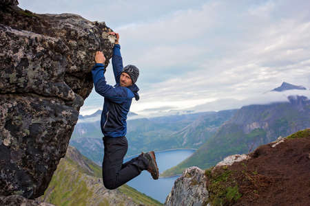 Happy child, hanging from a rock over Segla mountain on Senja island, North Norway. Amazing beautiful landscape and splendid nature in scandinavian country Norwayの写真素材