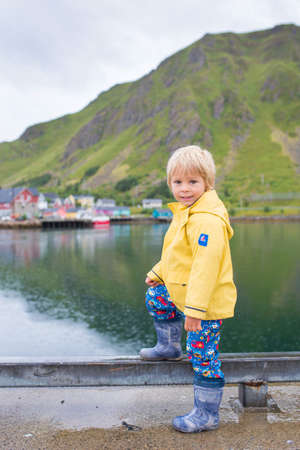 Cute child, boy, watching the typical Rourbuer fishing cabins in Lofoten village on a rainy day,...