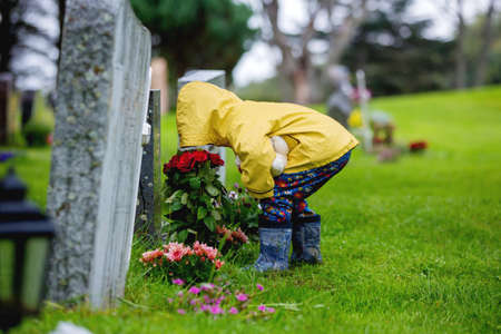 Sad little child, blond boy, standing in the rain on cemetery, sad person, mourning, summer rainy dayの写真素材
