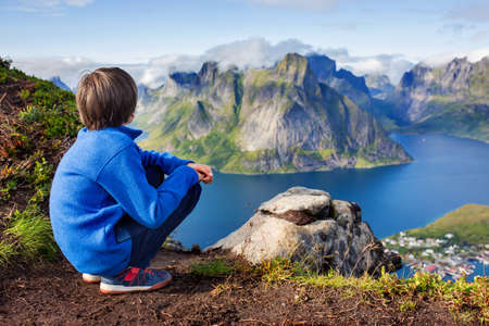 Cute child, standing on top of the mountains and looking down on Reine after climbing Reinebringen treeking path with lots of stairsの写真素材