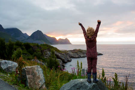 Cute child, enjoying amazing view from a rock in Husoy on Senja island, North Norway. Amazing...