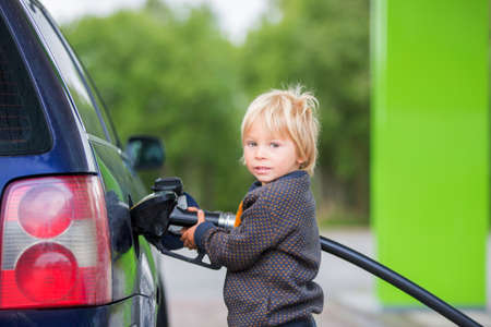 Sweet little child, blond boy, helping parents to put fuel in the car on a gas station, little champ helpingの写真素材