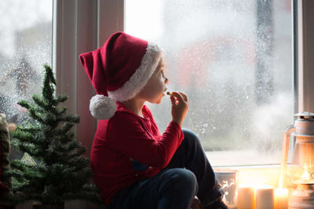 Beautiful toddler child, boy, waiting on the window on Christmas eve, looking for Santa Claus curiouslyの写真素材
