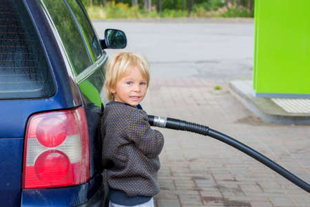 Sweet little child, blond boy, helping parents to put fuel in the car on a gas station in Swedenの写真素材