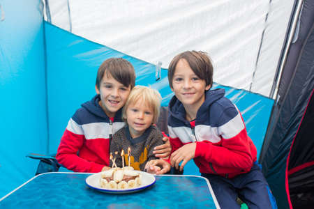 Twelve years old boy, celebrating his birthday with small improvised cake with candles in a tent on...