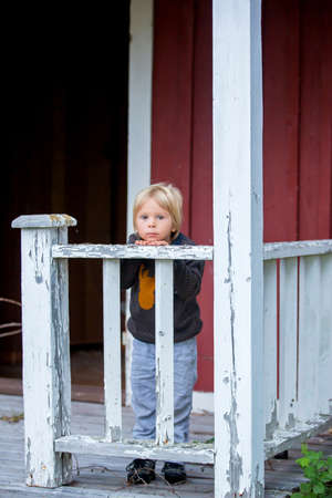 Sad little child, preschool boy, sitting on stairs in front of old ruined house, sadnessの写真素材