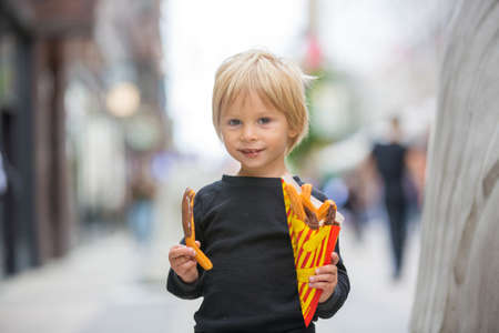 Cute blond child with black shirt, eating churros on the street in the city of Stockhlom, sweet desert sold on every corner of the cityの写真素材