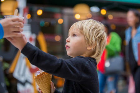 Cute blond child with black shirt, eating churros on the street in the city of Stockhlom, sweet desert sold on every corner of the cityの写真素材