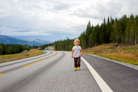 Beautiful blond child, standing in the middle of the highway on an empty road, running happily,...