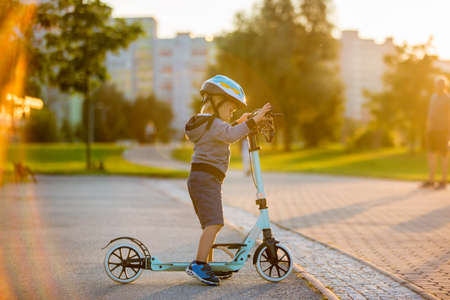 Cute preschool child, playing in the park on scooter on sunset, summertimeの写真素材