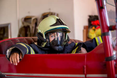 Child, cute boy, dressed in fire fighers cloths in a fire station with fire truck, childs dream