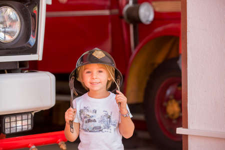 Child, cute boy, dressed in fire fighers cloths in a fire station with fire truck, childs dreamの写真素材